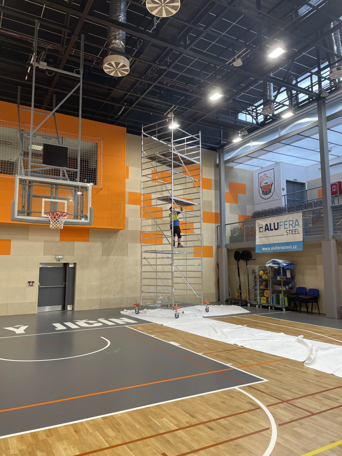 Pracovník při výměně osvětlení na lešení v basketbalové hale
