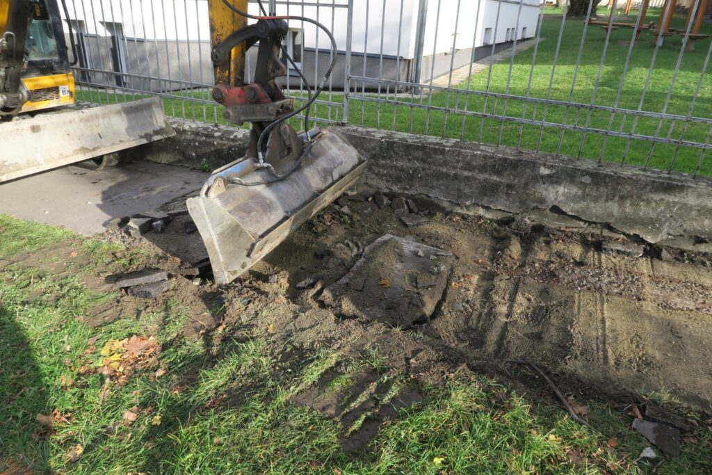 lžice bagru odstraňuje starý asfaltový chodník v Jiráskově ulici